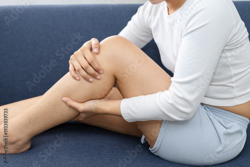 Valokuva Close up of women holding painful lower leg while sitting on sofa at home