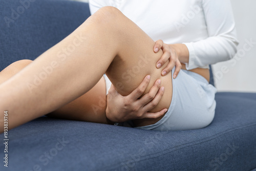 Photos Close up of women holding painful thigh while sitting on sofa at home
