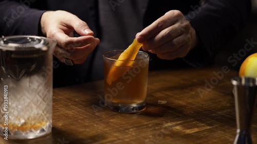 Bartender garnishing an old fashioned cocktail with an orange peel and serving.