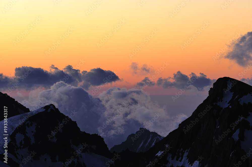 Αυτοκόλλητο Dramatic sunset light illuminates clouds above majestic snow-capped mountains