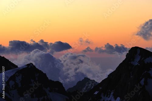 Fotografie Dramatic sunset light illuminates clouds above majestic snow-capped mountains