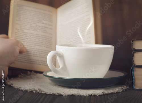 Cozy reading scene with cup of hot coffee, open book and steam on rustic wooden table