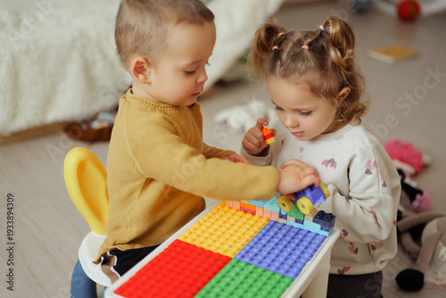 Two young children build and create with colorful plastic blocks at a table. They focus on their activity, enjoying playtime in a comfortable setting