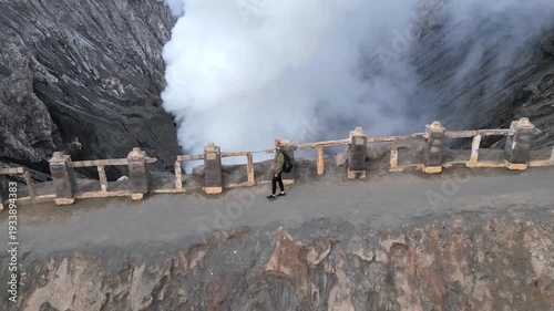 Aerial view of woman walking along the rim of steaming Mount Bromo volcano crater in Indonesia. Concept of nature, travel, adventure, and breathtaking landscapes.