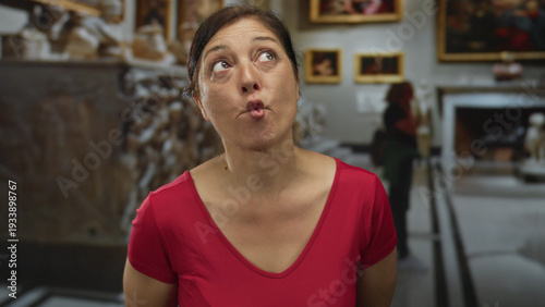 Принти на полотні Middle aged hispanic woman in bright red shirt forming cheeky fish face with lips in church interior; joy