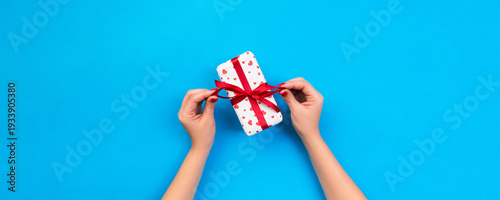 Wallpaper Mural Woman hands give wrapped valentine or other holiday handmade present in paper with red ribbon. Present box, red heart decoration of gift on blue table, top view with copy space for you design Torontodigital.ca