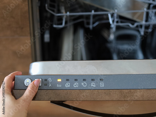 Slika na platnu Hand operating dishwasher control buttons with indicator lights on, concept of smart kitchen technology and automated cleaning