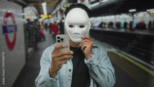 Bild auf Leinwand Man holding white mask near his face while gripping smartphone at train station platform building; anonymity