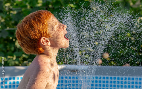 Red-haired child playing cheerfully with water in outdoor pool