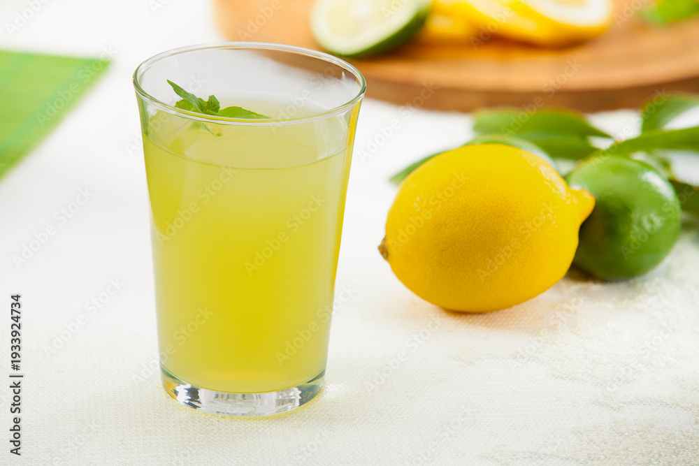Fototapeta premium Fresh homemade lemonade or lime juice in a glass with lemon and lime slices on a wooden board, bright garden background.