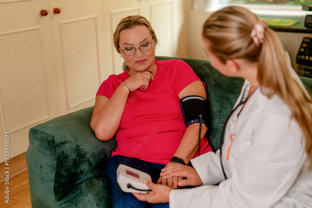 Fototapeta premium Health check at home with nurse assisting patient during routine blood pressure measurement
