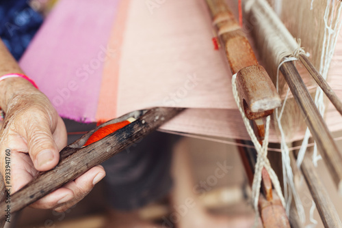 Thai woman weaving colorful silk fabric with ancient technique in rural village.