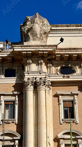 Architectural detail of historic Roman building facade with classical columns and sculptures under blue sky in Rome, Italy.