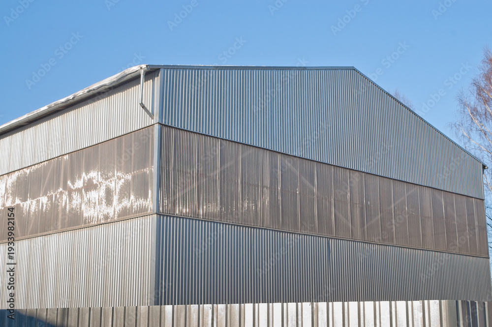 Fototapeta premium A close-up of a gray metal fence with a metal hangar and blue sky in the background