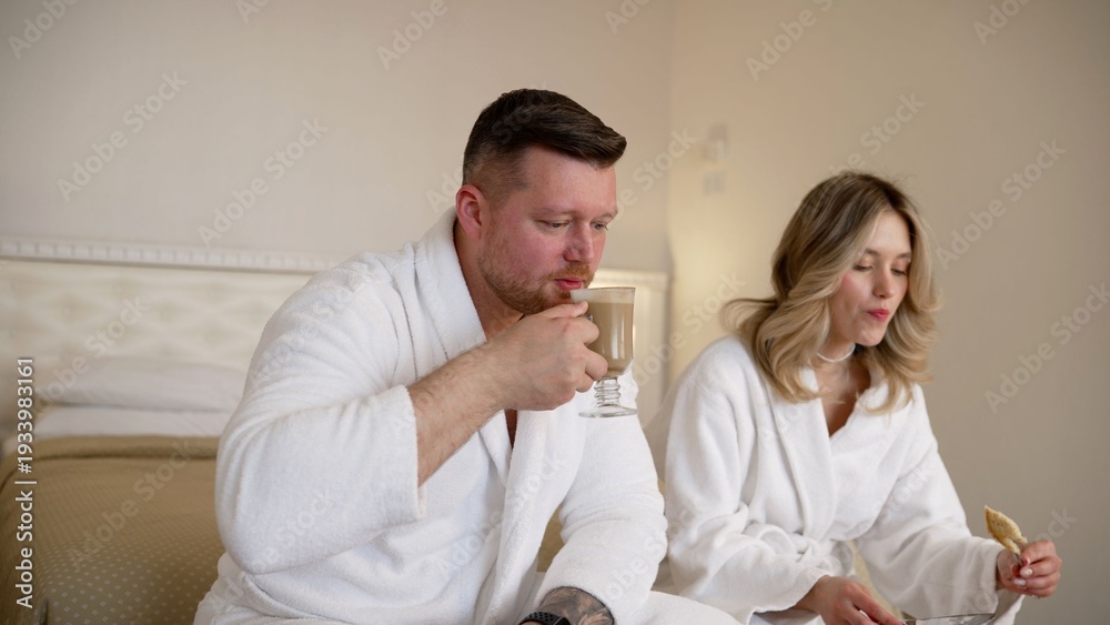 Fototapeta premium Couple in bathrobes enjoying a relaxed morning with coffee in a hotel room
