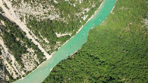 Stunning aerial shot of the turquoise Verdon river winding through lush green forest and rocky cliffs in the Verdon Gorge, France. Several small boats are visible on the water, highlighting outdoor