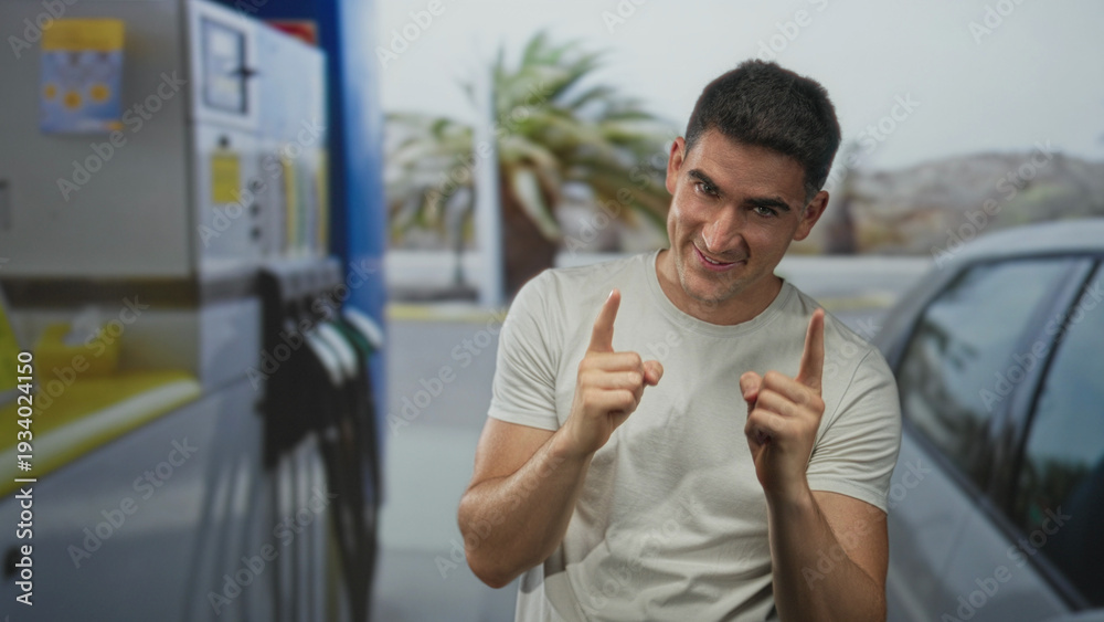 Fototapeta premium Man smiling and pointing finger toward camera at petrol pump beside silver car on street; confidence playful.
