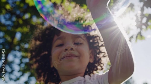 black girl blowing bubbles in park sunlight, curly hair, white dress, green trees, sun flare, iridescent giant bubble, low angle perspective, joyful smile, summer meadow, carefree play, slow motion