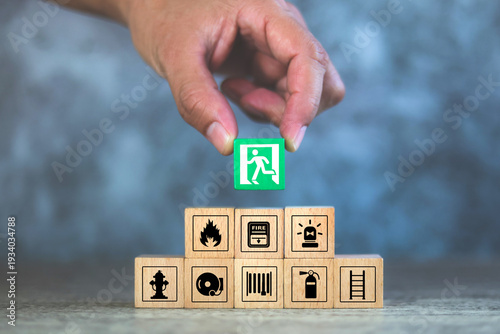 Hand choose cube wooden block stack with fire prevent icon and door exit sing or escape with fire extinguisher and emergency protection symbol for safety and rescue in the building.