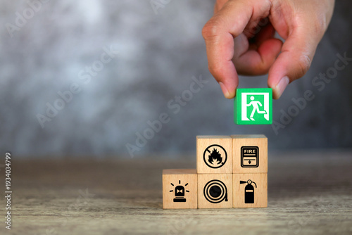 Hand choose cube wooden block stack with fire prevent icon and door exit sing or escape with fire extinguisher and emergency protection symbol for safety and rescue in the building.