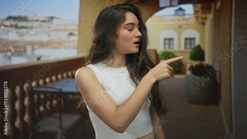 Canvas Print Woman in white tank top pointing finger to side in sunlit building hallway with serious gaze; rejection