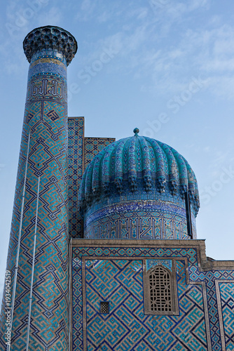 Sher Dor Madrasah turquoise dome and azure minaret fragment. Intricate mosaic tiles, geometric patterns, calligraphy bands and ribbed cupola under blue sky. Registan Square, Samarkand, Uzbekistan.