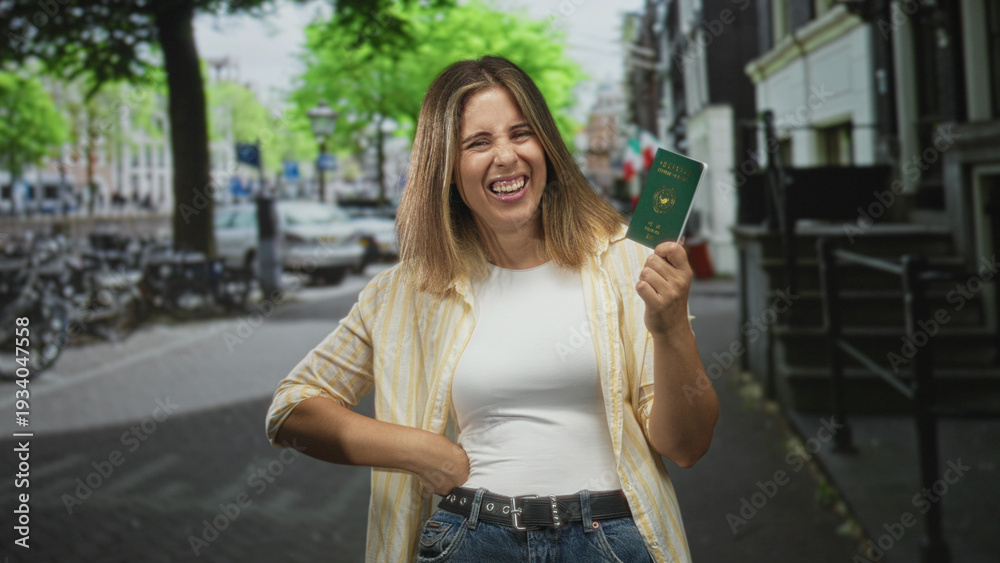 Fototapeta premium Woman holding passport up, hand on hip, smiling and looking sideways in street with bicycles and buildings; joy travel freedom.