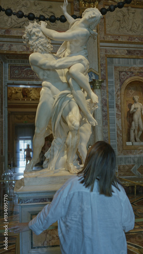 Wallpaper Mural Young woman with hand on railing leaning forward viewing large marble statue of two figures in ornate gallery building; art appreciation awe. Torontodigital.ca