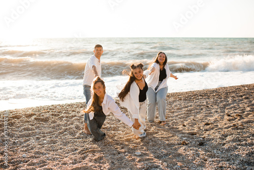 Happy family of four persons: mother, dad and two daughters having fun at beach over sea background. Summer vacation season.
