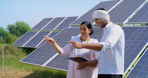 Indian mature adult woman hold tab look visit farm field do work check record data at rural area ground place female talk speak share eco friendly solar panel power plan idea to young male