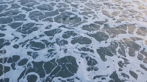 Ocean waves create dynamic foam patterns on the water surface, showcasing the continuous movement and flow of the sea in a coastal environment
