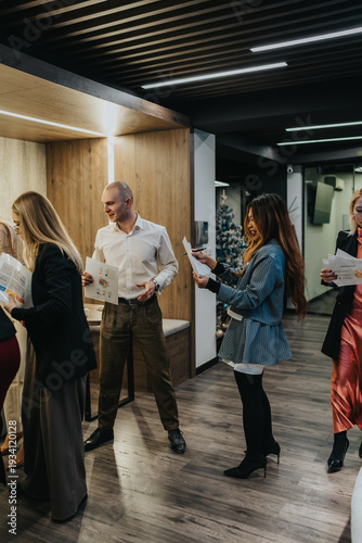 Wallpaper Mural A group of professionals interact and review papers in a sleek, contemporary office. The scene conveys collaboration and a festive, office atmosphere with a Christmas tree in the background. Torontodigital.ca