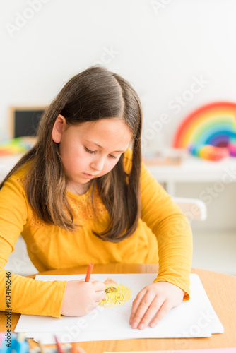 Little girl using crayons to paint while homeschooling wearing a yellow shirt in a bright and colorful home