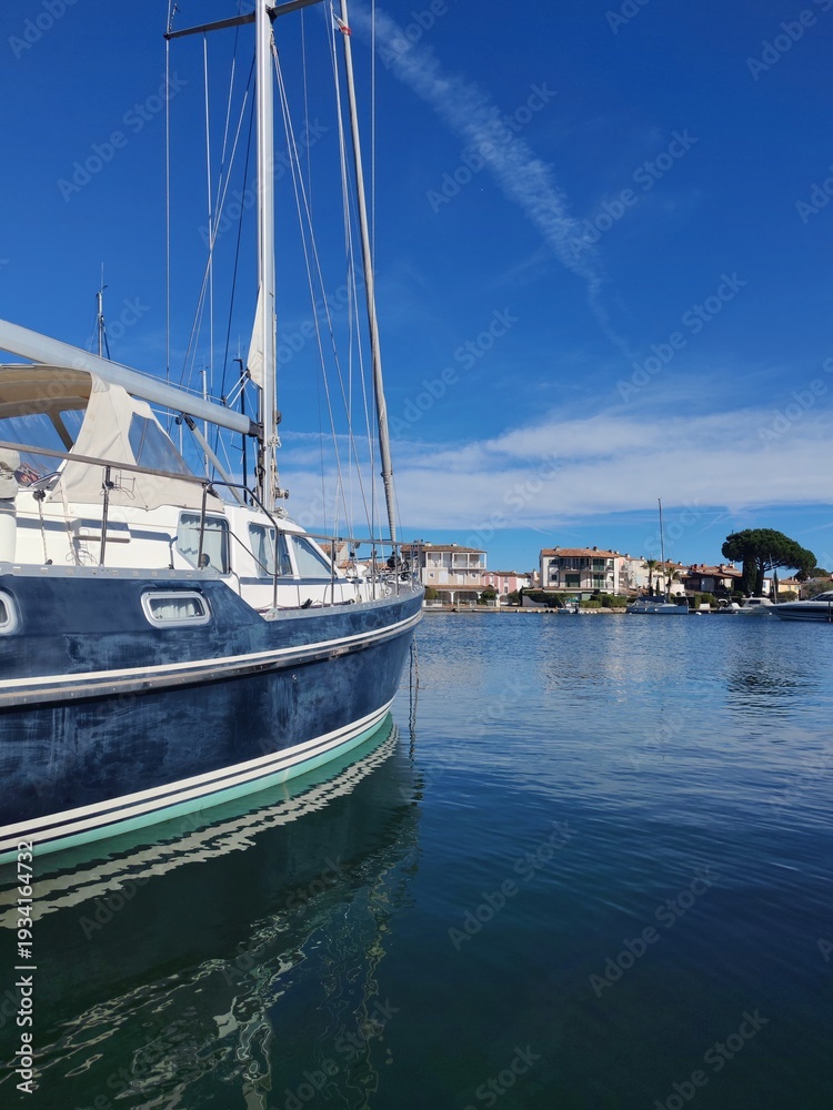 Fototapeta premium Grimaud,France - Febrary 18,2026:Blue yaht moored on calm water, where it reflected, at the Grimaud port