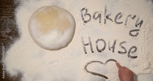 Принти на полотні Baker prepares dough and writes bakery house name in flour on wooden table