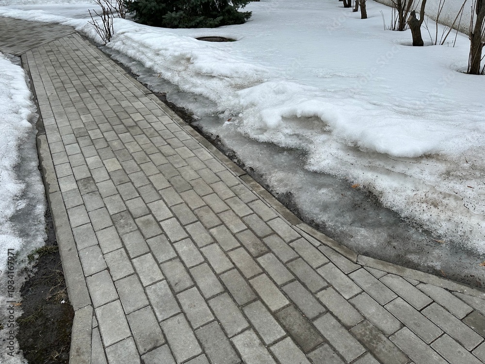 Naklejka premium Paving stone sidewalk with melting dirty snow on the sides