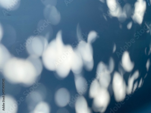 Soft light bokeh on blue background abstract nature shadows. Abstract background featuring soft out-of-focus light spots and natural leaf shadows on a blue surface.