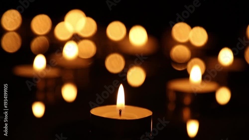A candle burns in the foreground, the flame flickers and bends slightly over the frames. Warm golden bokeh lights float behind and pulsate softly, creating a cozy nighttime atmosphere.
