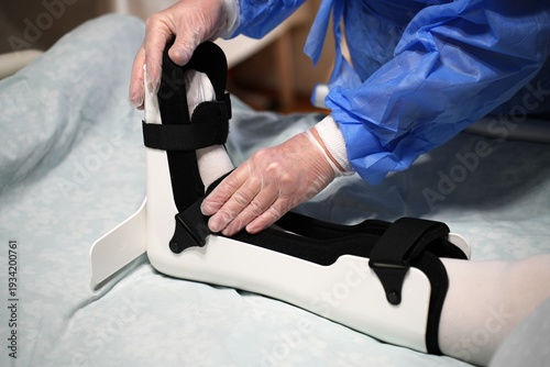 Medical Professional Adjusting Ankle Orthosis Brace. Doctor carefully correcting the fit of a orthopedic ankle foot orthosis (AFO) for a patient in a hospital bed. Focused on clinical rehabilitation
