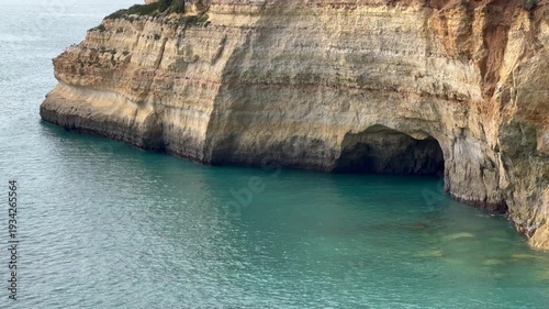 View of the sea and rocky coastline framed by the entrance of a coastal cave. The natural composition combines ocean water, rugged cliffs, and clear blue sky, symbolizing exploration and scenic beauty