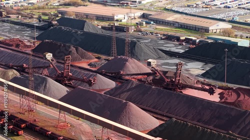 Aerial drone view of massive coal and iron ore stockpiles at Immingham Port, UK, featuring heavy industrial machinery and port operations.