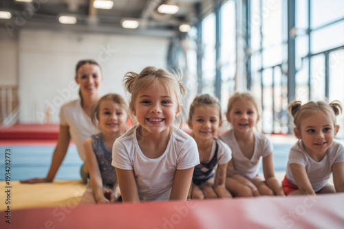 children learning gymnastics from coach in modern gym, bright interior, natural light, engaged and smiling kids.