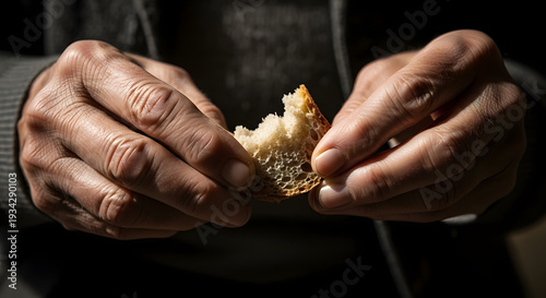 Close-up of a person's hands breaking a piece of rustic bread, with dramatic lighting highlighting the texture and gesture.