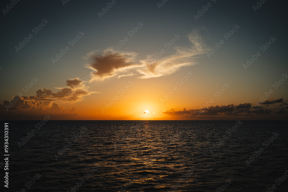 Obraz premium Beautiful sunset over a calm dark ocean with golden clouds