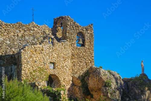 Ancient stone chapel surrounded by greenery against a bright blue sky