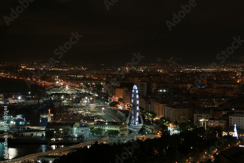 Panoramic night view of a coastal city with a Ferris wheel and harbor lights