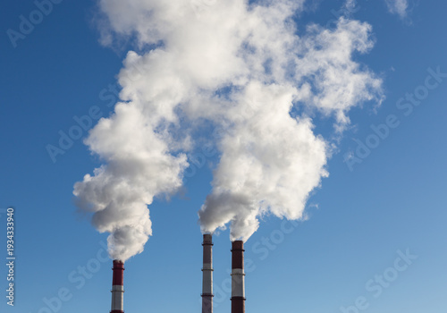 CHP emissions. Smoking chimney releasing smoke against a blue sky. Smoke from factory pipe of heat station in the city. Air pollution. Nuclear power plant cooling. CO2, greenhouse gases emissions.