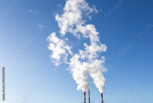 CHP emissions. Smoking chimney releasing smoke against a blue sky. Smoke from factory pipe of heat station in the city. Air pollution. Nuclear power plant cooling. CO2, greenhouse gases emissions.
