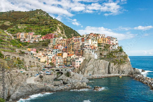 Scenic view of Manarola along Cinque Terre with colorful houses on a rocky coastline above the Mediterranean Sea in Liguria, Italy against blue sky with clouds
