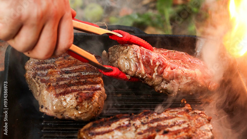 Obraz na płótnie Juicy beef steaks sizzling on a cast iron grill pan with flames licking the side
